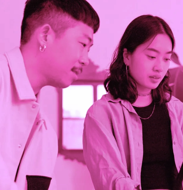 Two people in conversation, pink tinted image, with obscured faces.