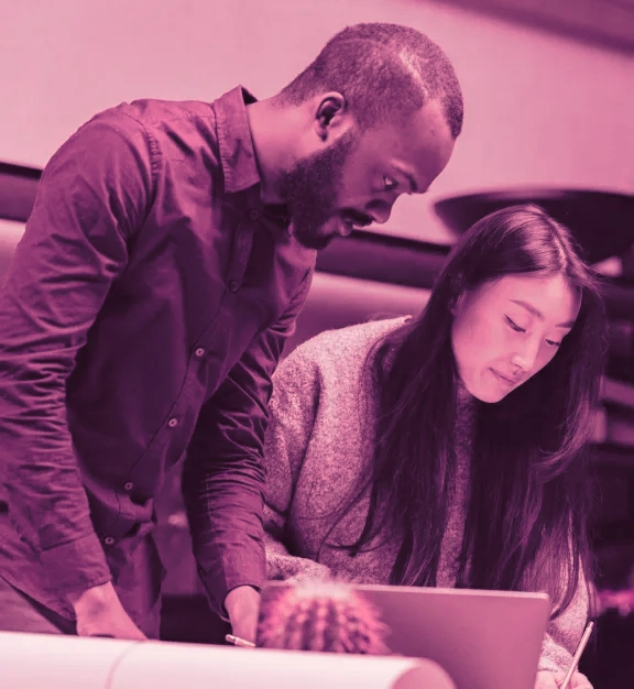 Two individuals collaborating over a laptop with a monochrome pink filter.
